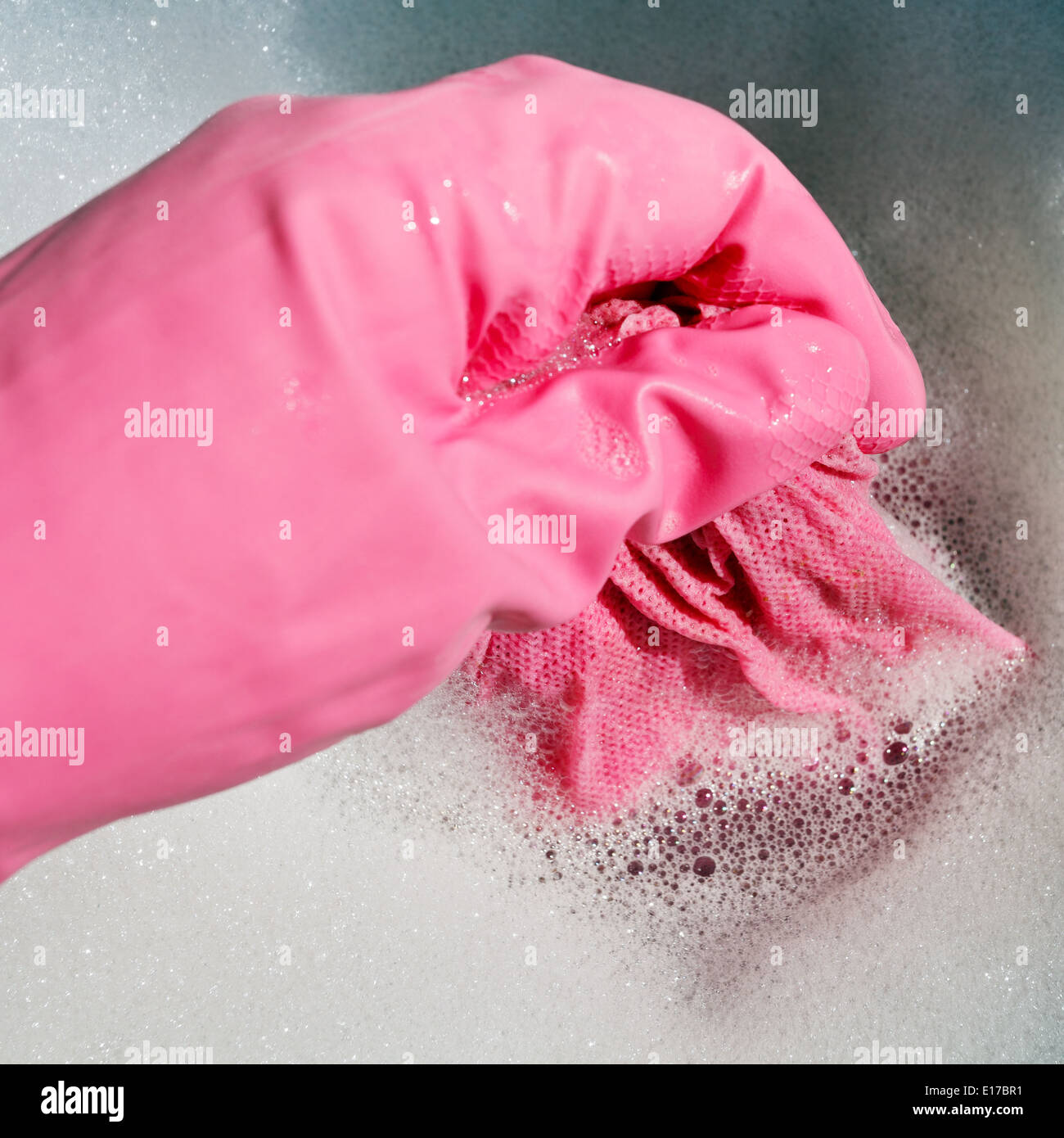 Hand in rosa Gummihandschuh ringt, nasses Tuch aus dem schäumenden Wasser Stockfoto