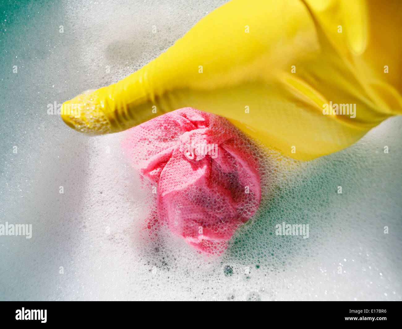 Hand im gelben Gummihandschuh ringt, nasses Tuch aus dem schäumenden Wasser Stockfoto