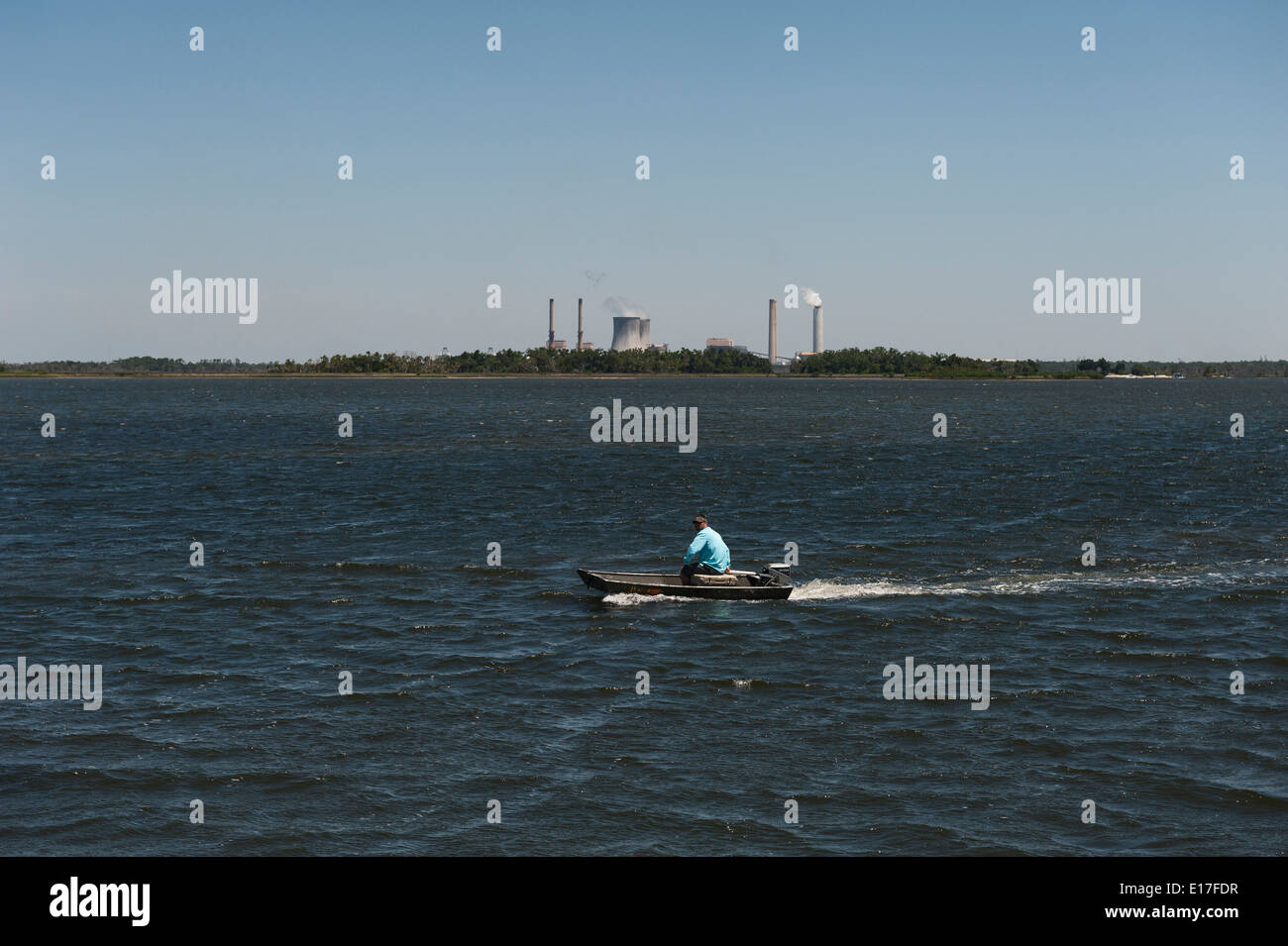 Ein Mann in einem Boot auf Crystal River Florida mit dem Crystal River Kernkraftwerk im Hintergrund. Stockfoto