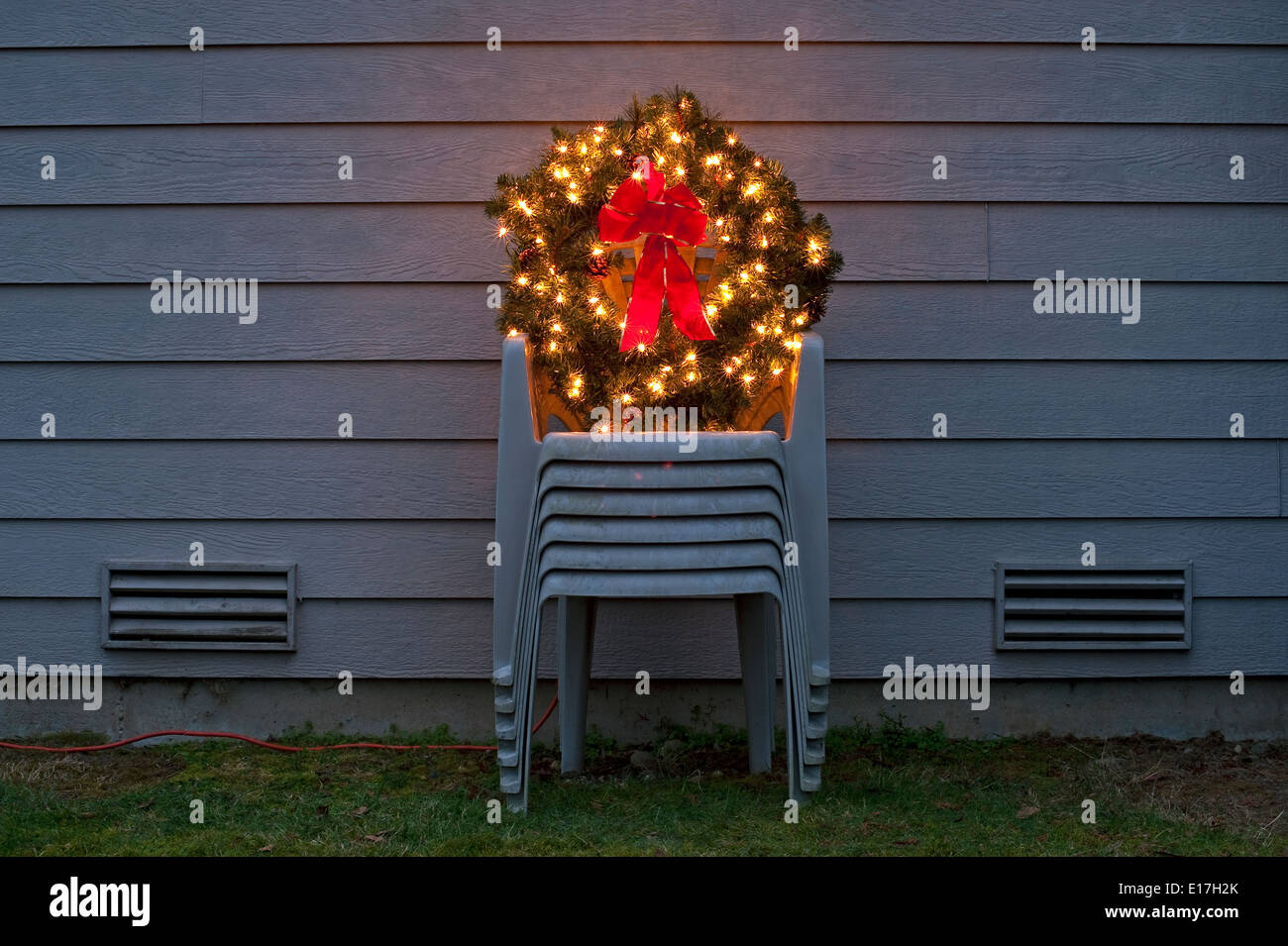 Weihnachtskranz in Hinterhof auf gestapelte Gartenmöbel mit Weihnachtsbeleuchtung und roter Schleife Stockfoto