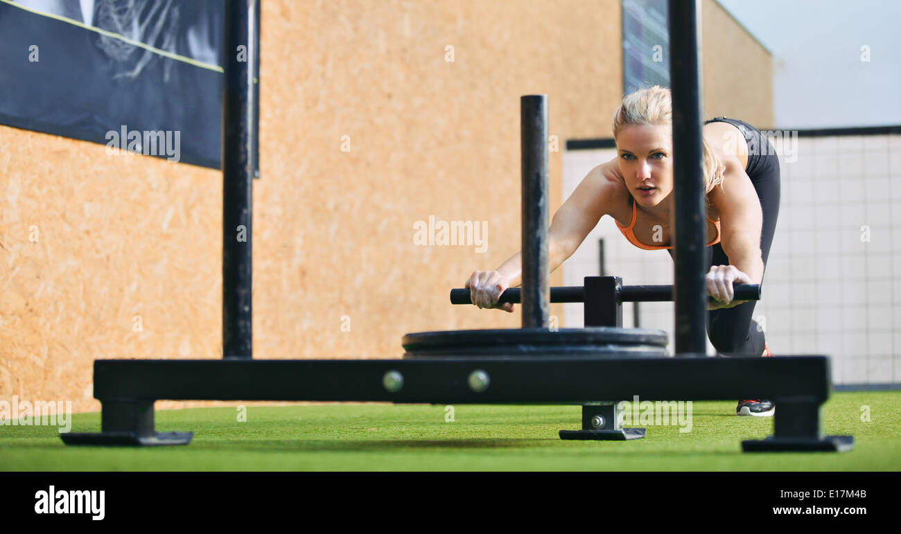 Muskulös und kräftig junges Weibchen Drücken der Prowler Sportgeräte auf Kunstrasen Rasen. Fit Woman auszuüben. Stockfoto