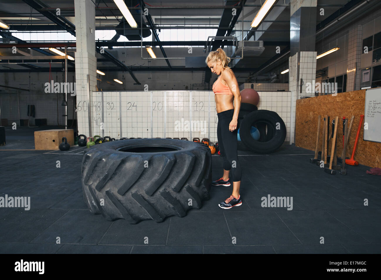 Starke junge Frau Sportler stehen und blickte auf riesigen Reifen im Fitnessstudio. Passen Sie die Sportlerin Reifen spiegeln Übung durchführen. Stockfoto