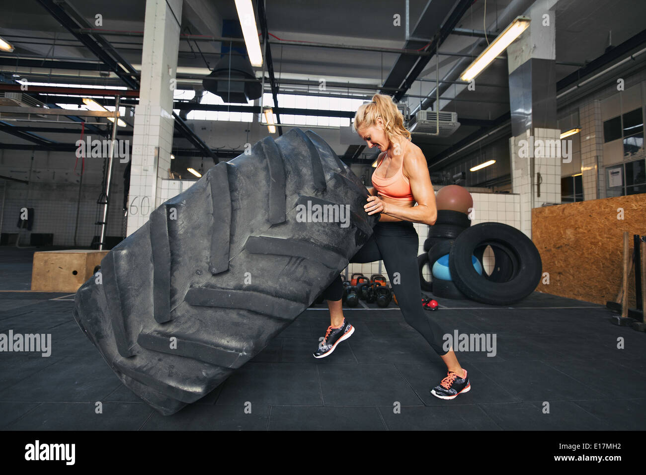Muskulöse junge Frau spiegeln Reifen im Fitnessstudio. Fit Sportlerin, die Durchführung eines Reifens flip bei Crossfit Gym. Stockfoto
