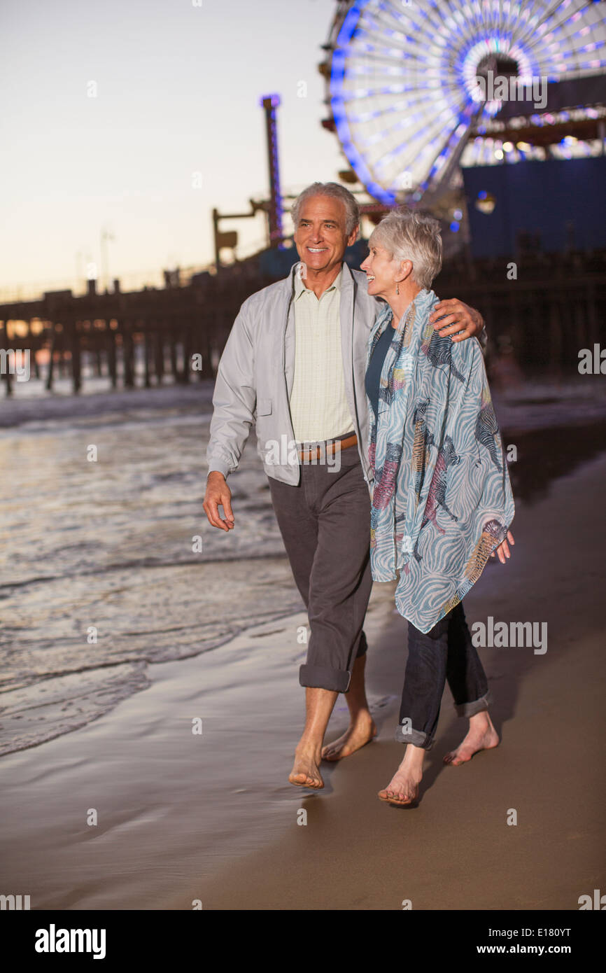Älteres Paar zu Fuß am Strand bei Sonnenuntergang Stockfoto