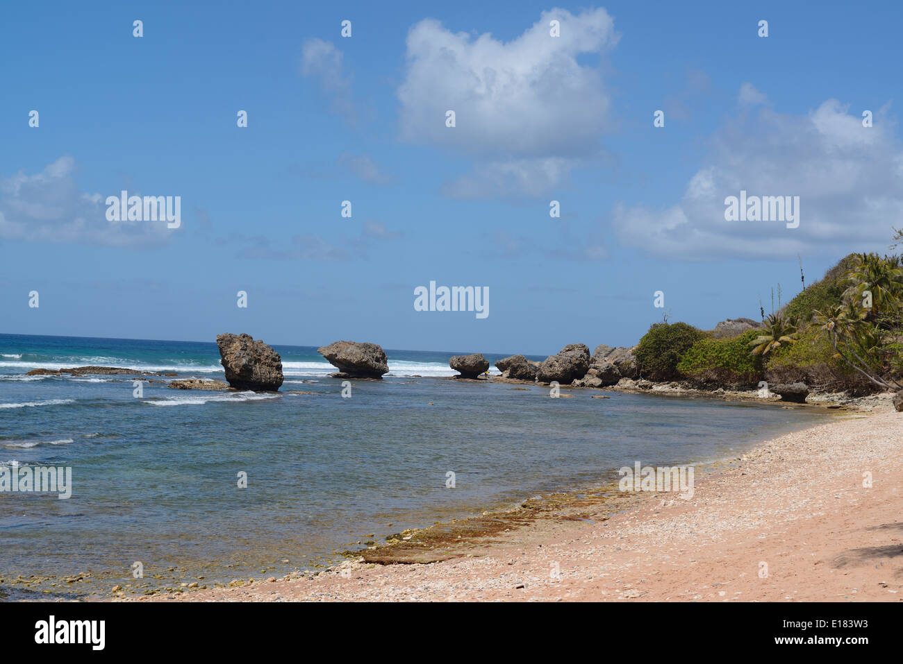 Ein Kiesstrand mit Felsen hinter unter einem hellen Sommerhimmel auf der Insel Barbados Stockfoto