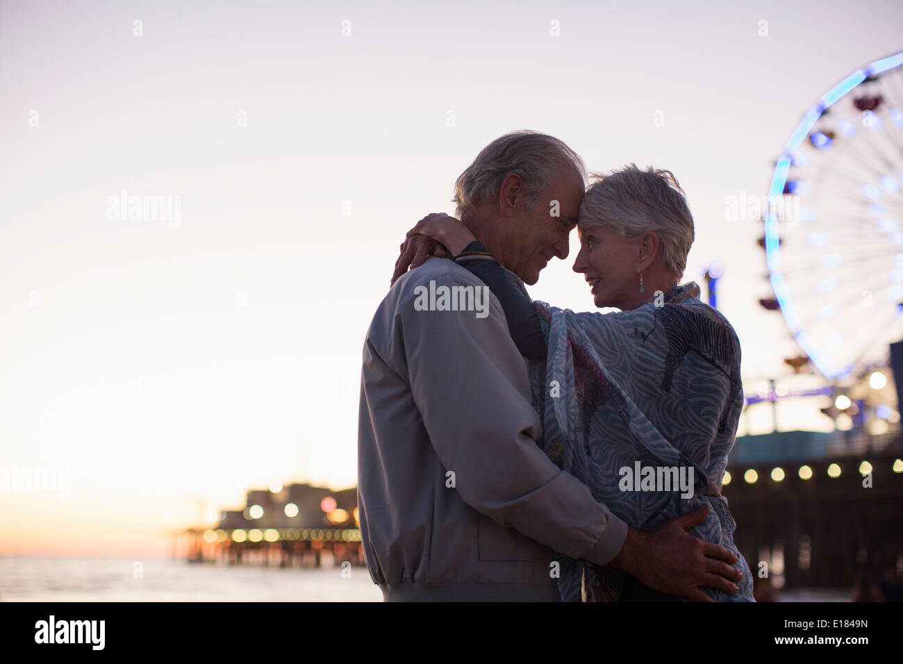 Älteres paar umarmt am Strand bei Sonnenuntergang Stockfoto
