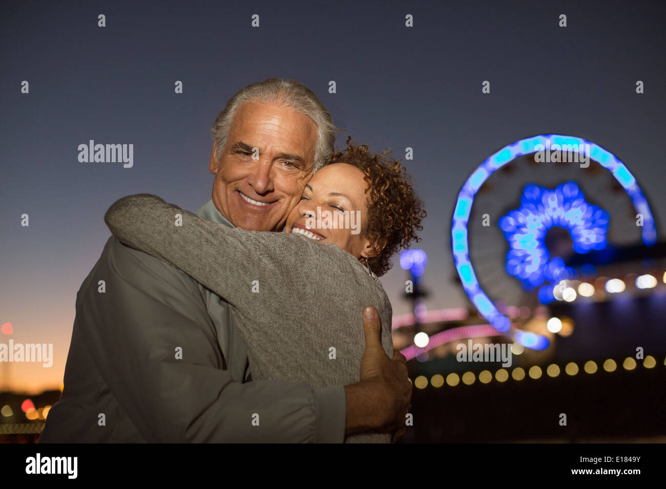 Porträt von paar umarmt außerhalb Vergnügungspark in der Nacht Stockfoto