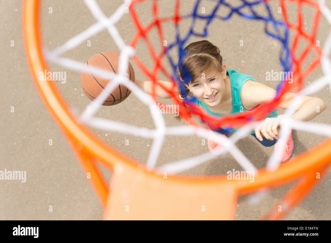 Blick von oben durch das Netz eine lächelnde junge Teenager weiblichen Basketball-Shooter nehmen sollen den Ball für ein Ziel zu werfen Stockfoto