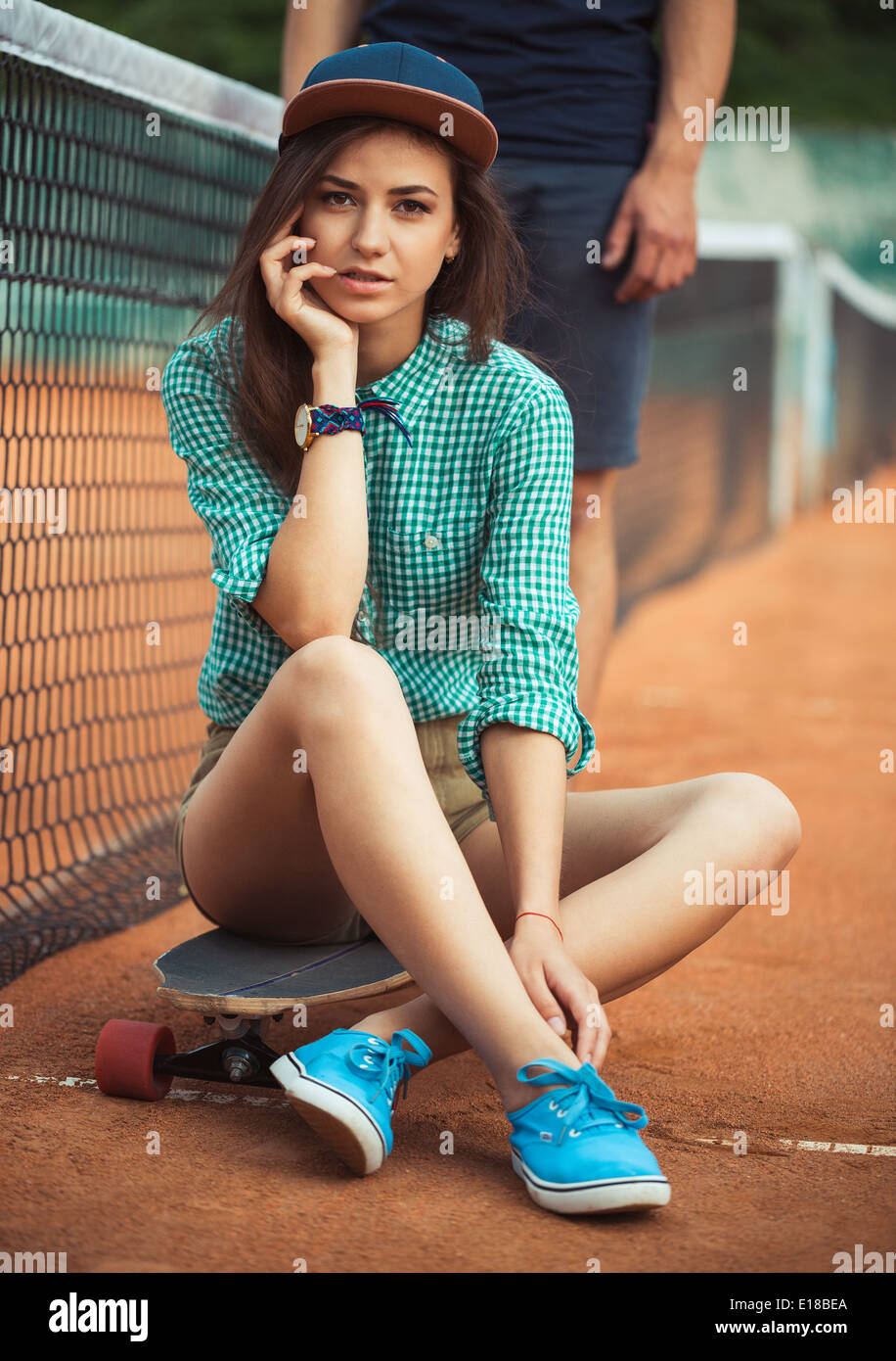 Junge schöne Mädchen sitzen auf einem Skateboard auf dem Tennisplatz Stockfoto