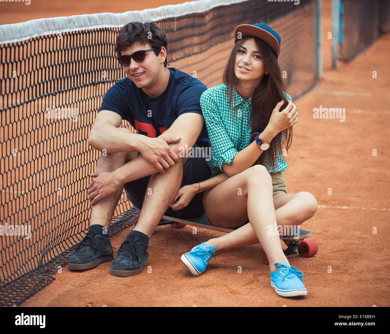 Junge schöne Paar sitzt auf einem Skateboard auf dem Tennisplatz Stockfoto