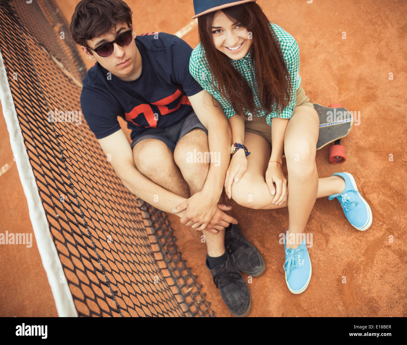 Junge schöne Paar sitzt auf einem Skateboard auf dem Tennisplatz Stockfoto