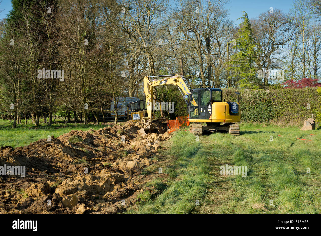 Bagger in einem Feld mit Graben für unterirdische Stromkabel Stockfoto