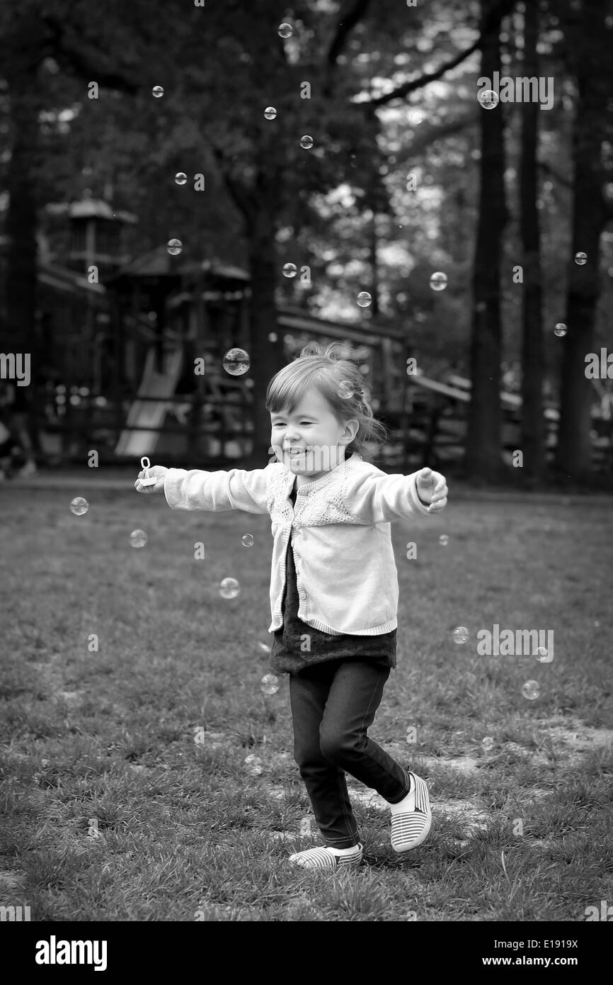 Ein Lächeln auf den Lippen 2 Jahres altes Mädchen läuft durch den Park, umgeben von Luftblasen Stockfoto