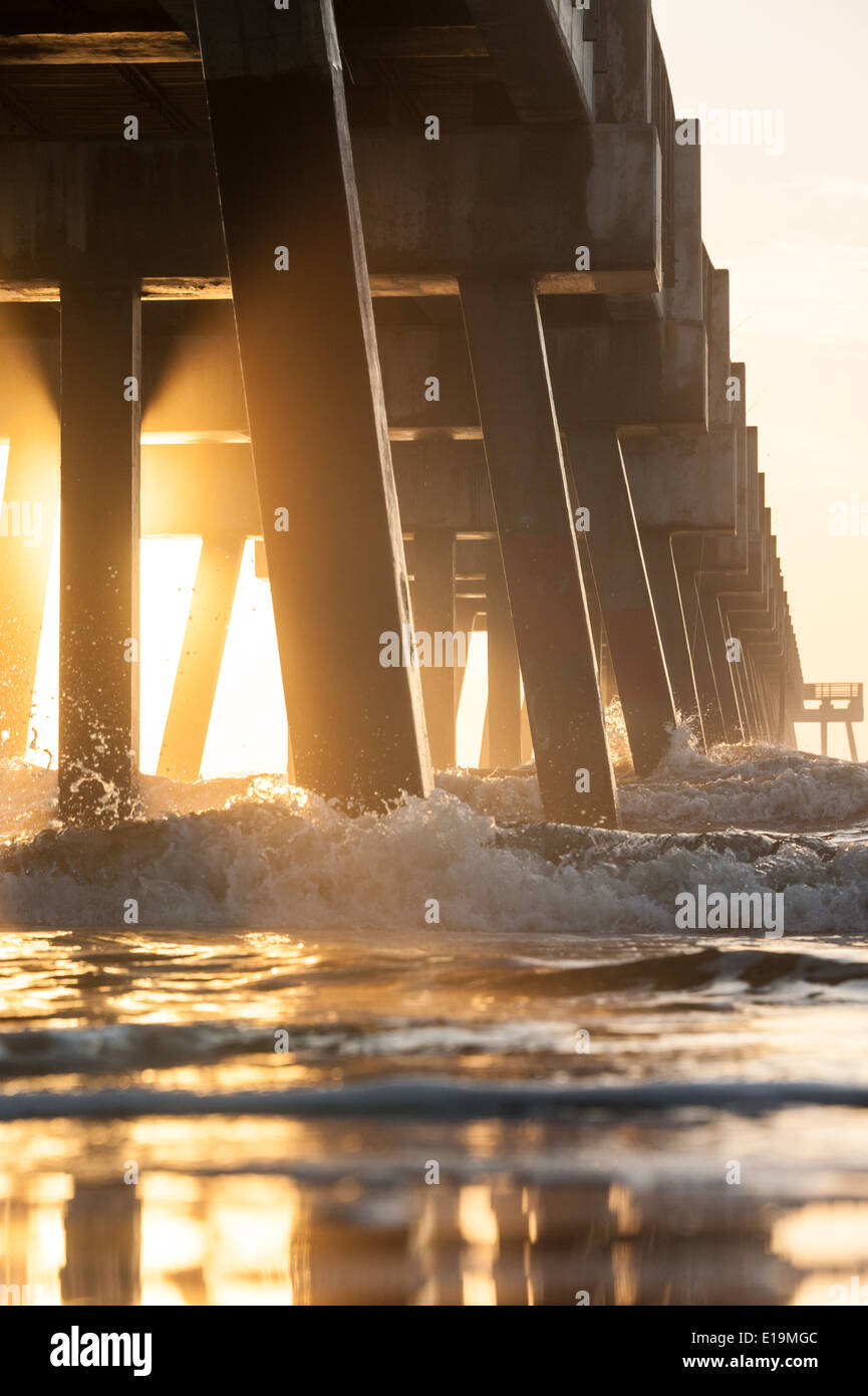 Die aufgehende Sonne beleuchtet einen am frühen Morgennebel unter der Jacksonville Beach Pier im Nordosten Florida/USA. Stockfoto