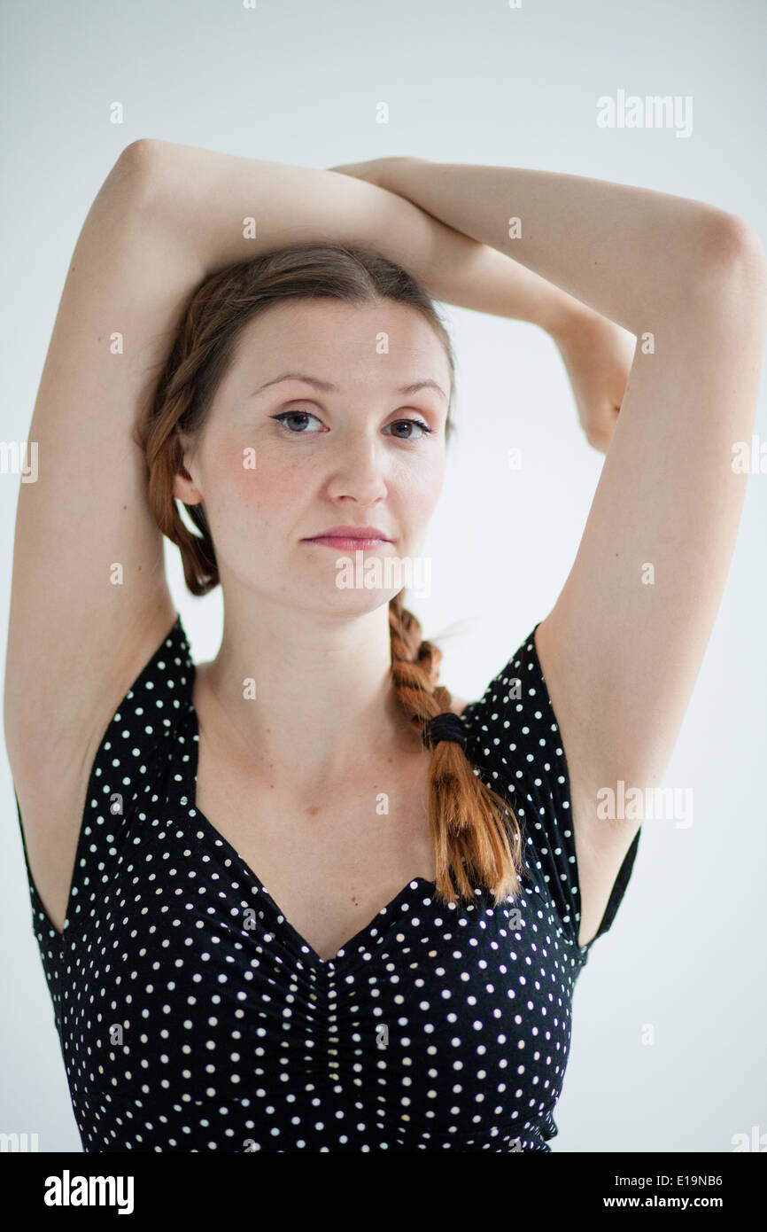 Studioportrait von entspannt suchen attraktive Frau mit Zopf tragen nicht so doll dunkle Bluse posiert mit Arme über Kopf Stockfoto