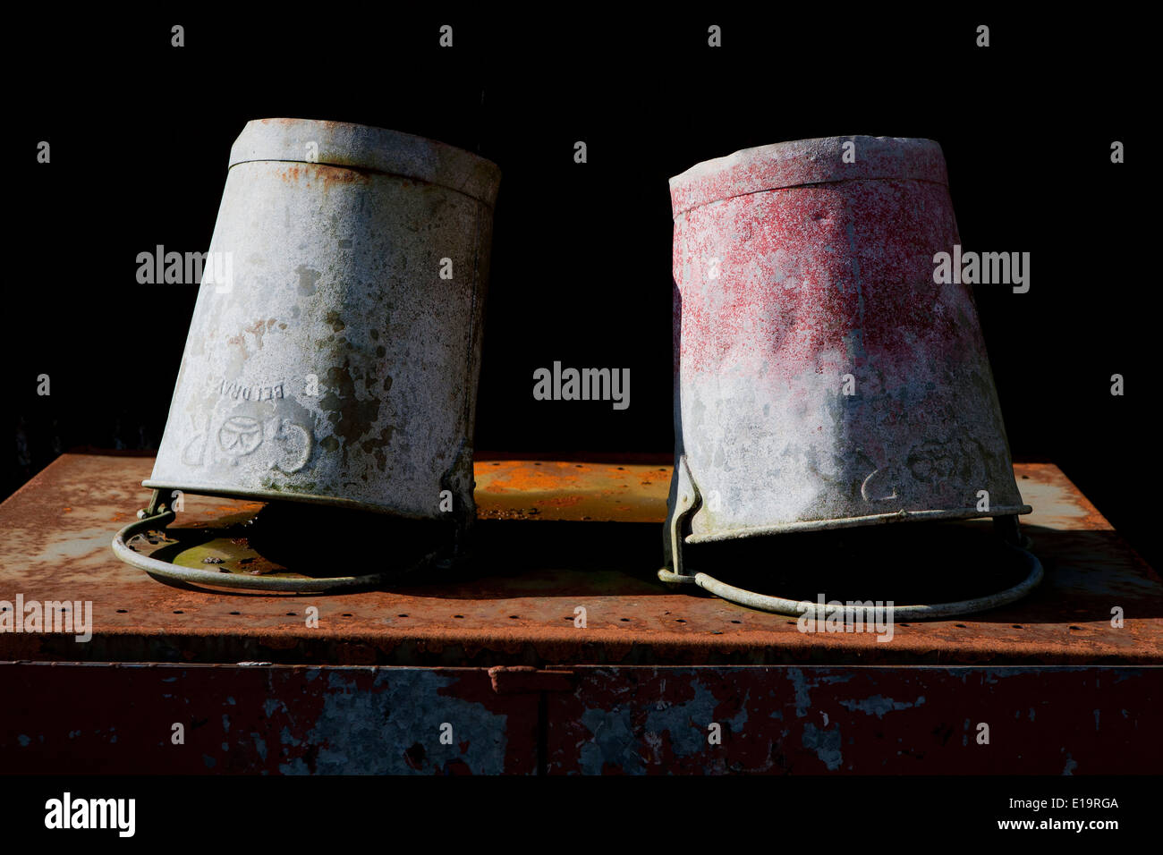 Zwei verzinkte Eimer mit verblassten Farben ruht auf dem Kopf stehend auf rostigen Metall. Stockfoto
