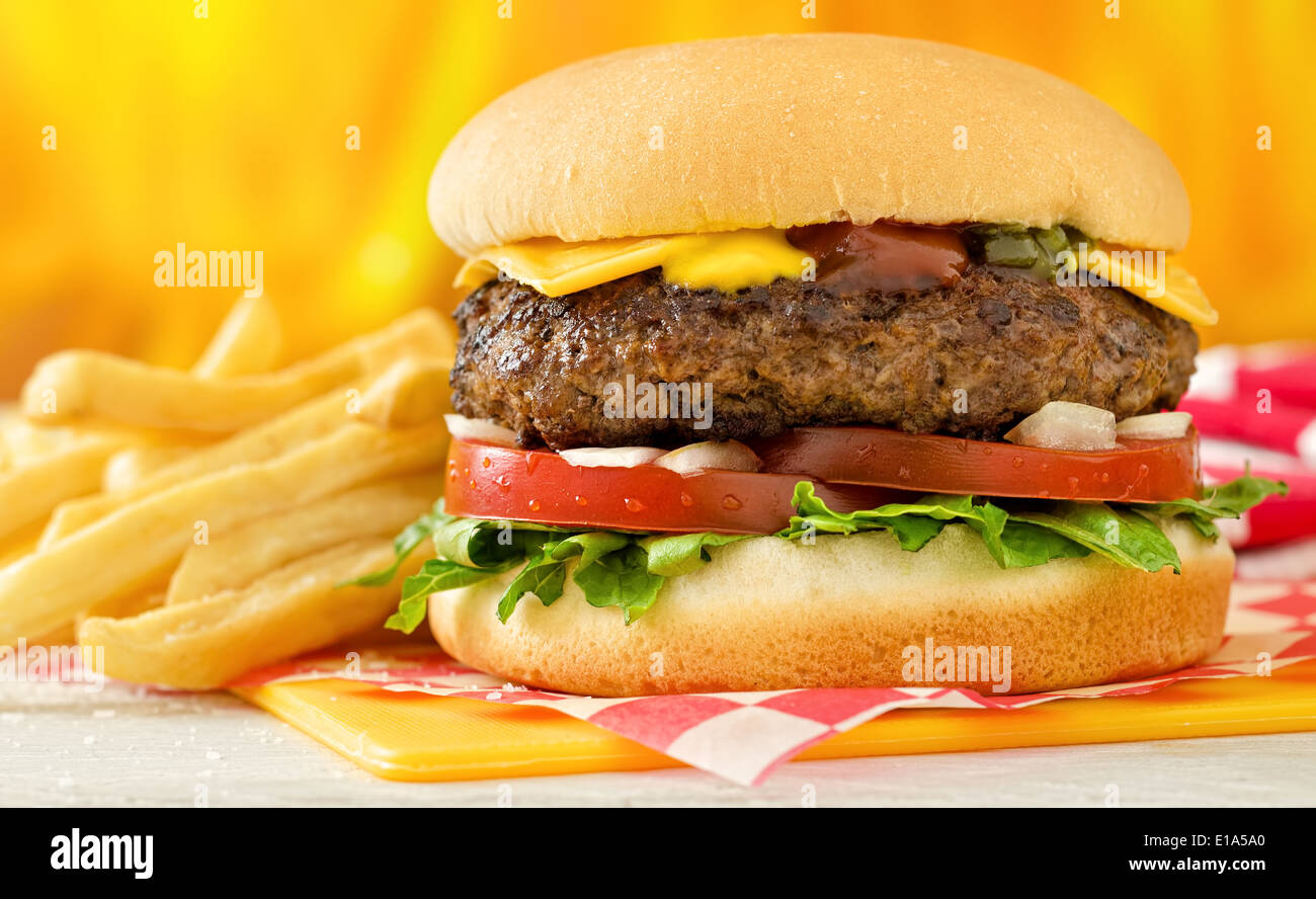 Einen klassischen Stil Cheeseburger mit Rindfleisch, Käse, Salat, Tomaten, Zwiebel, Senf, Ketchup und lustvoll mit Pommes Frites. Stockfoto