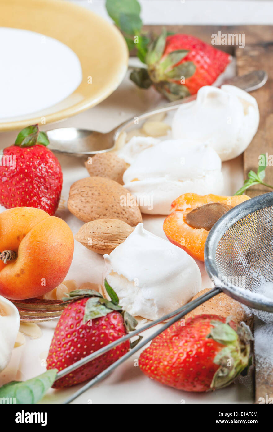 Hausgemachtes Baiser mit Aprikosen, Erdbeeren, Mandeln und Sahne. Zutaten für den Nachtisch Eton Chaos. Stockfoto
