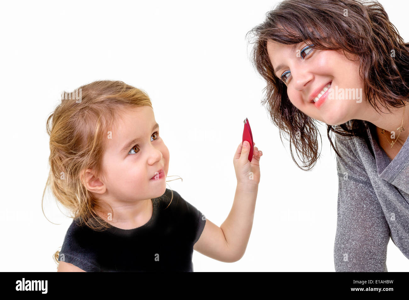 Niedliche kleine Mädchen mit einem spielerischen Ausdruck wollen ihre Mütter Make-up hält es in der Hand als ihre Mutter-Kurven Stockfoto