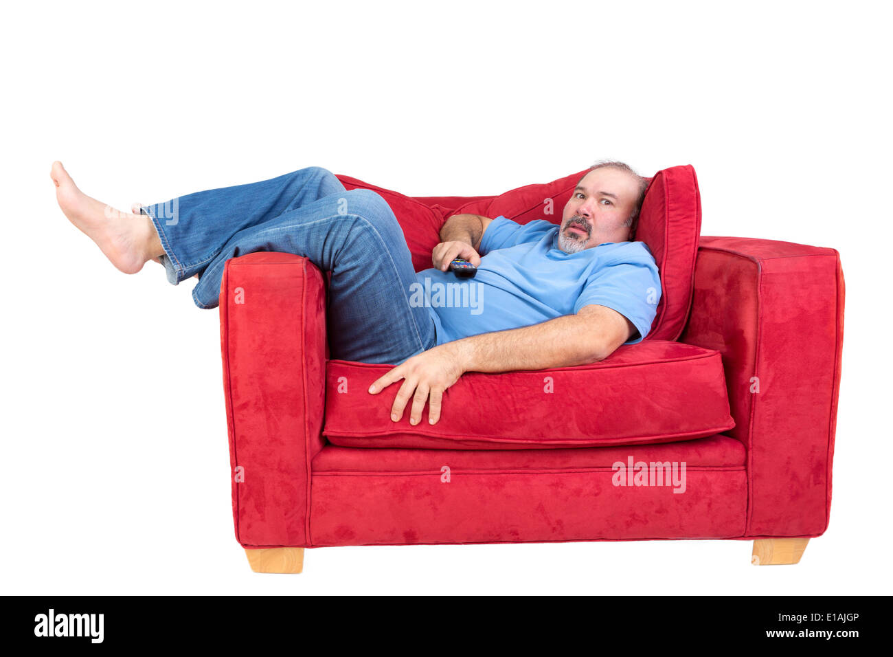 Mann in vor dem Fernseher liegen auf einem roten Sofa mit der Fernbedienung in der Hand und einen Blick von barfuß vertieft fasziniert Stockfoto