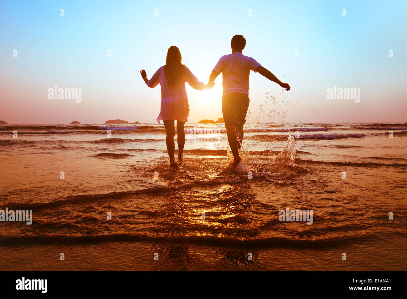 junge Brautpaar laufen ins Meer bei Sonnenuntergang Strand Stockfoto