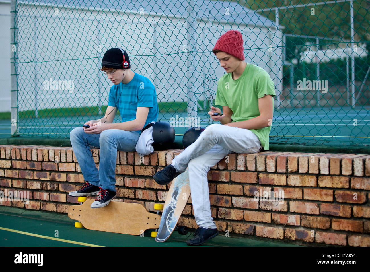 Skater sitzt auf einer Mauer, einer Musik hören, ist der andere mit Handy Stockfoto