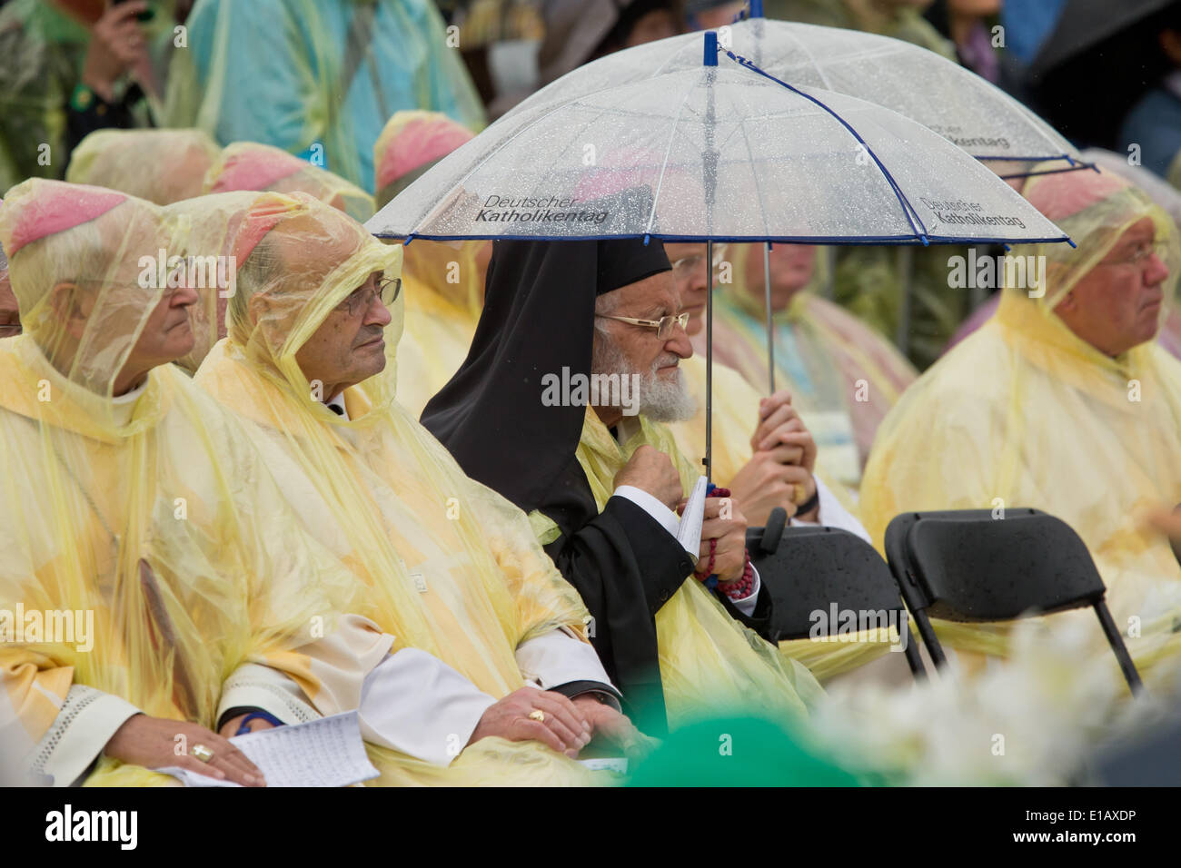 Regensburg, Deutschland. 29. Mai 2014. Mitglieder des Klerus tragen transparente Regenmäntel oder kauern unter Sonnenschirmen gegen Regenschauer besuchen die Himmelfahrt Masse bei der 99. Deutschen Katholikentag in Regensburg, Deutschland, 29. Mai 2014. Die Veranstaltung dauert bis 01 Juni. Foto: DANIEL KARMANN/Dpa/Alamy Live News Stockfoto
