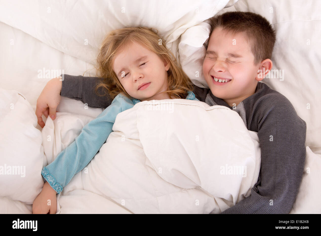 Zwei süße kleine Kinder miteinander schlafen teilen das gleiche Bett mit einem kleinen Jungen schützend, seine jüngere Schwester kuscheln Stockfoto