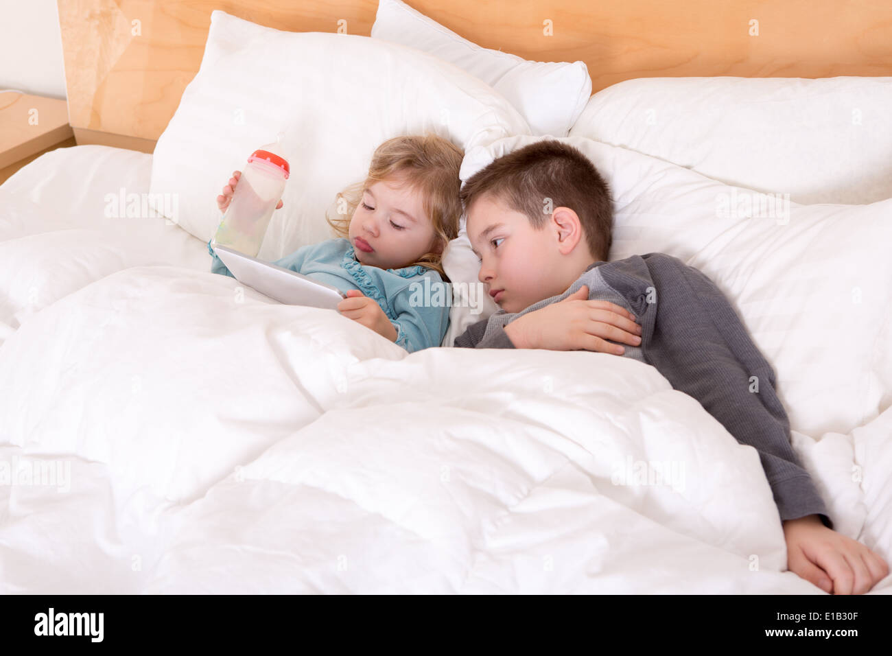 Glücklichen kleinen Bruder und Schwester zusammen im Bett liegen, wie sie kuscheln unter der Bettdecke Lesen eines Tablet-Computers vor dem Schlafengehen s Stockfoto