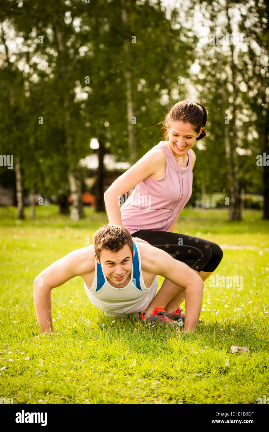 Sportler, die Liegestütze machen, während Frau auf ihm als ein Gewicht sitzt Stockfoto