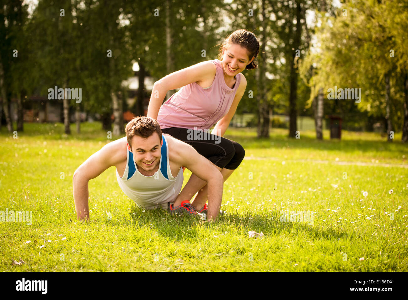 Sportler, die Liegestütze machen, während Frau auf ihm als ein Gewicht sitzt Stockfoto