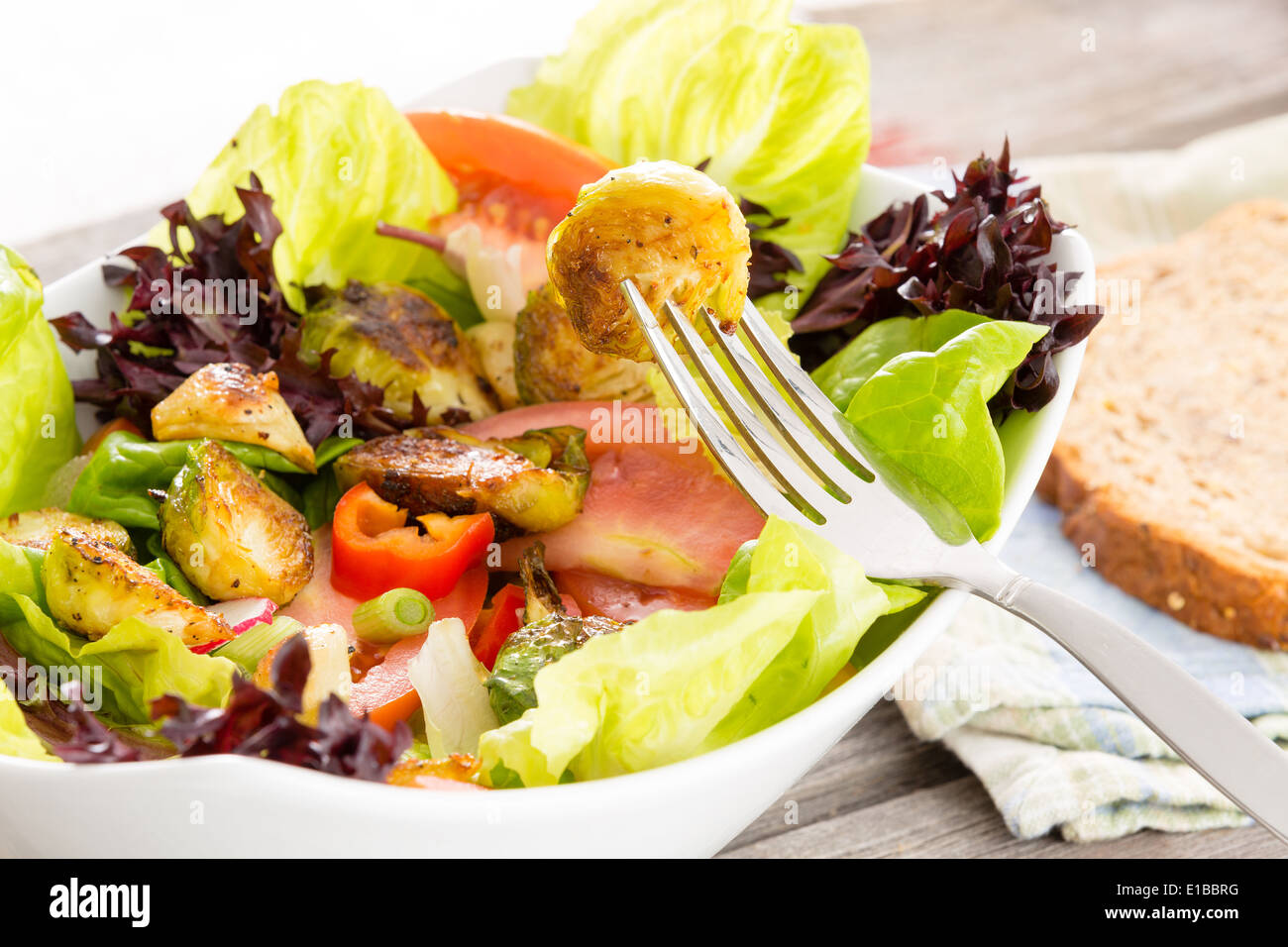 Genießen Sie eine gesunde vegetarische Mahlzeit sautierten Rosenkohl in einem Salat von gemischten Blattgemüse, Tomaten und Radieschen mit einer Scheibe Stockfoto