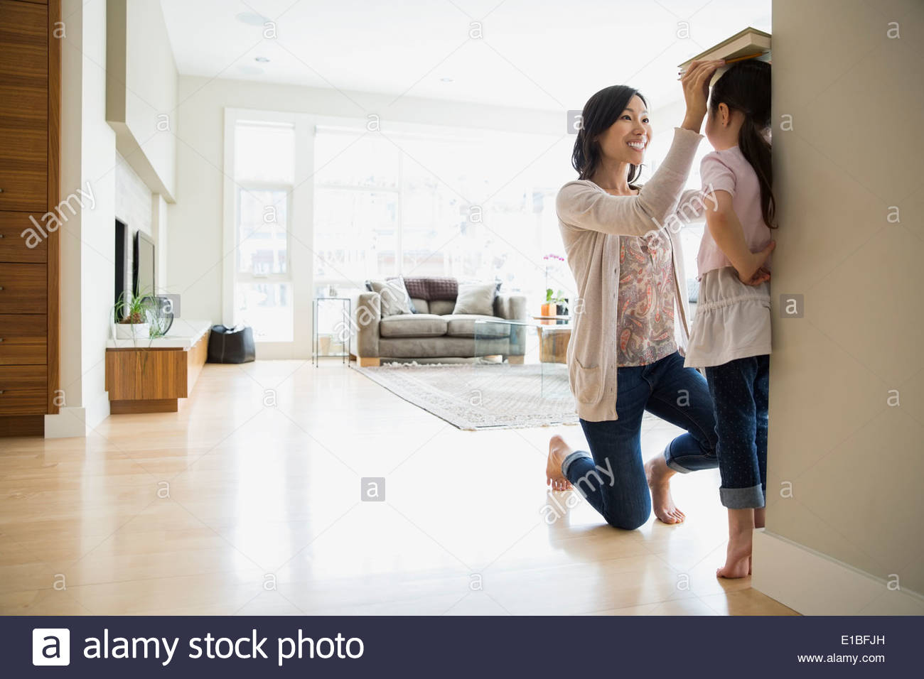 Mutter, die Messung der Höhe der Töchter im Wohnzimmer Stockfoto