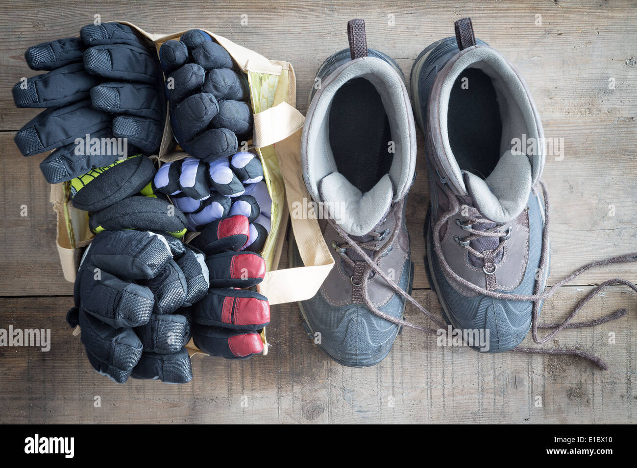 Schneestiefel mit den Schnürsenkeln liegen frei und einer Tasche Winterhandschuhe und Fäustlinge nebeneinander auf dem Boden von einem rustikalen bereit stehen Stockfoto