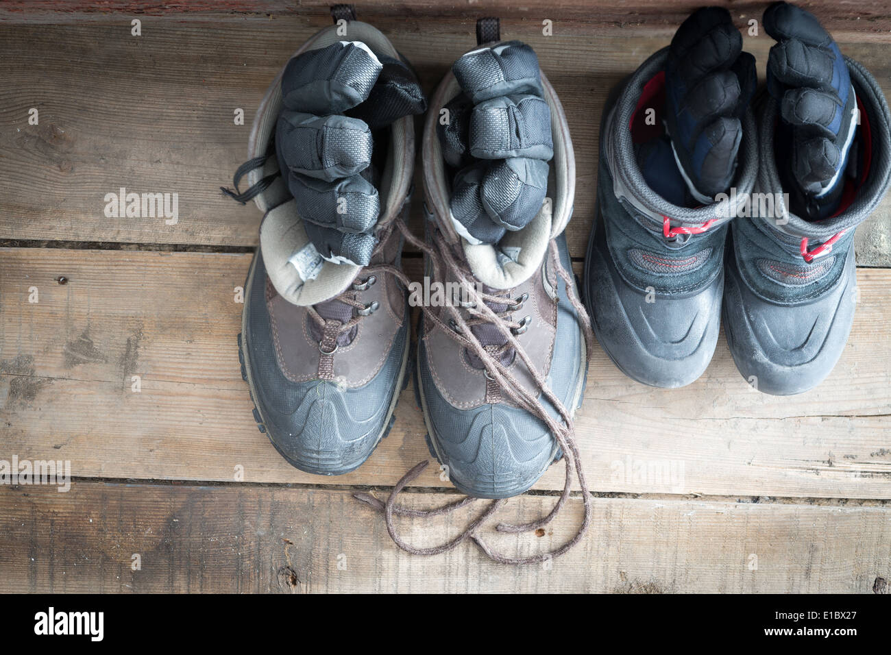 Ansicht von oben aus einem Paar von Erwachsenen Winterstiefel neben denen eines Kindes auf dem Holzboden eine Kabine mit Paar Handschuhe Stockfoto