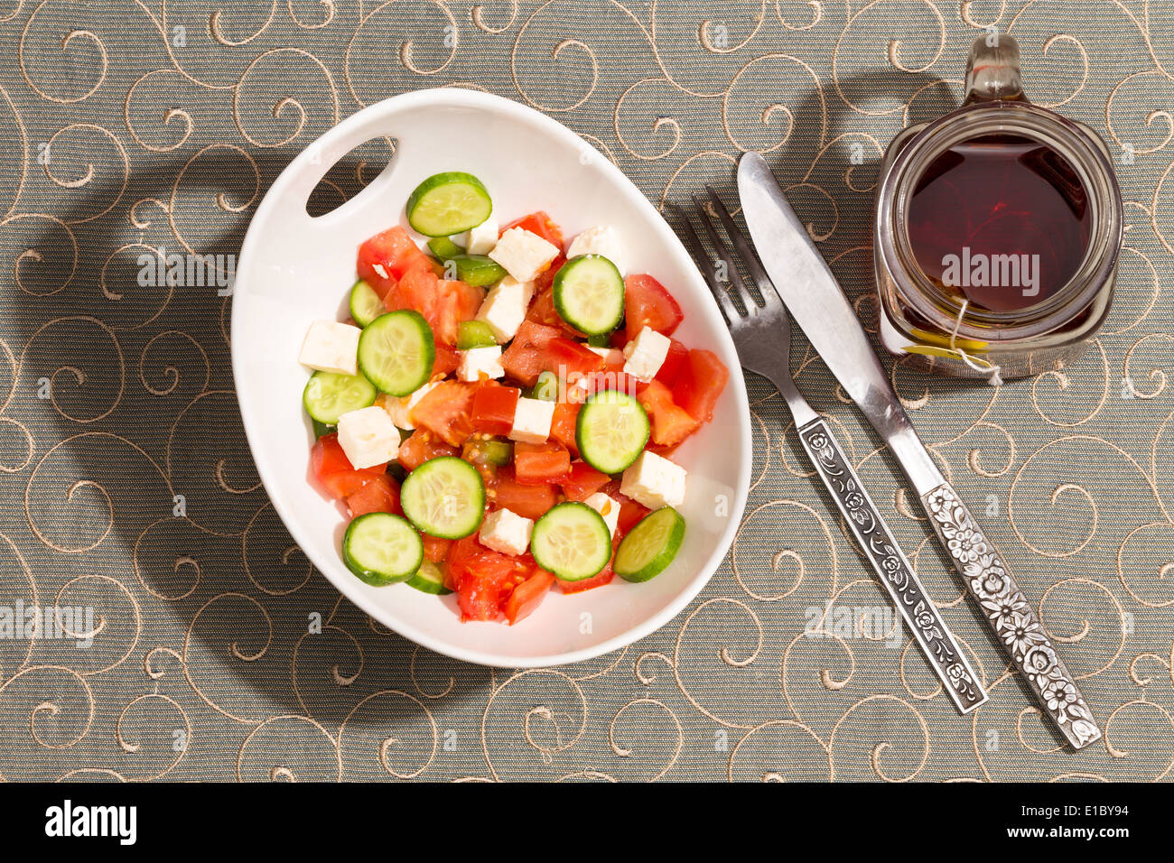 Gesunde frische Feta-Salat mit Käsewürfel, Gurken, Tomaten und grüne Paprika serviert mit einer Tasse heißem Tee auf eine hübsche pa Stockfoto