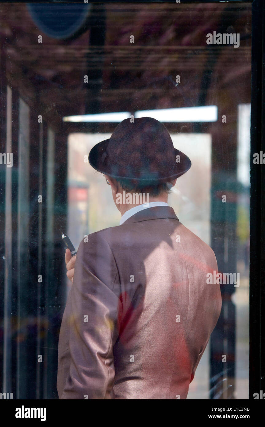 Ein Mann mit Trilby-Hut stand im Busunterstand und hielt E-Zigarette Stockfoto