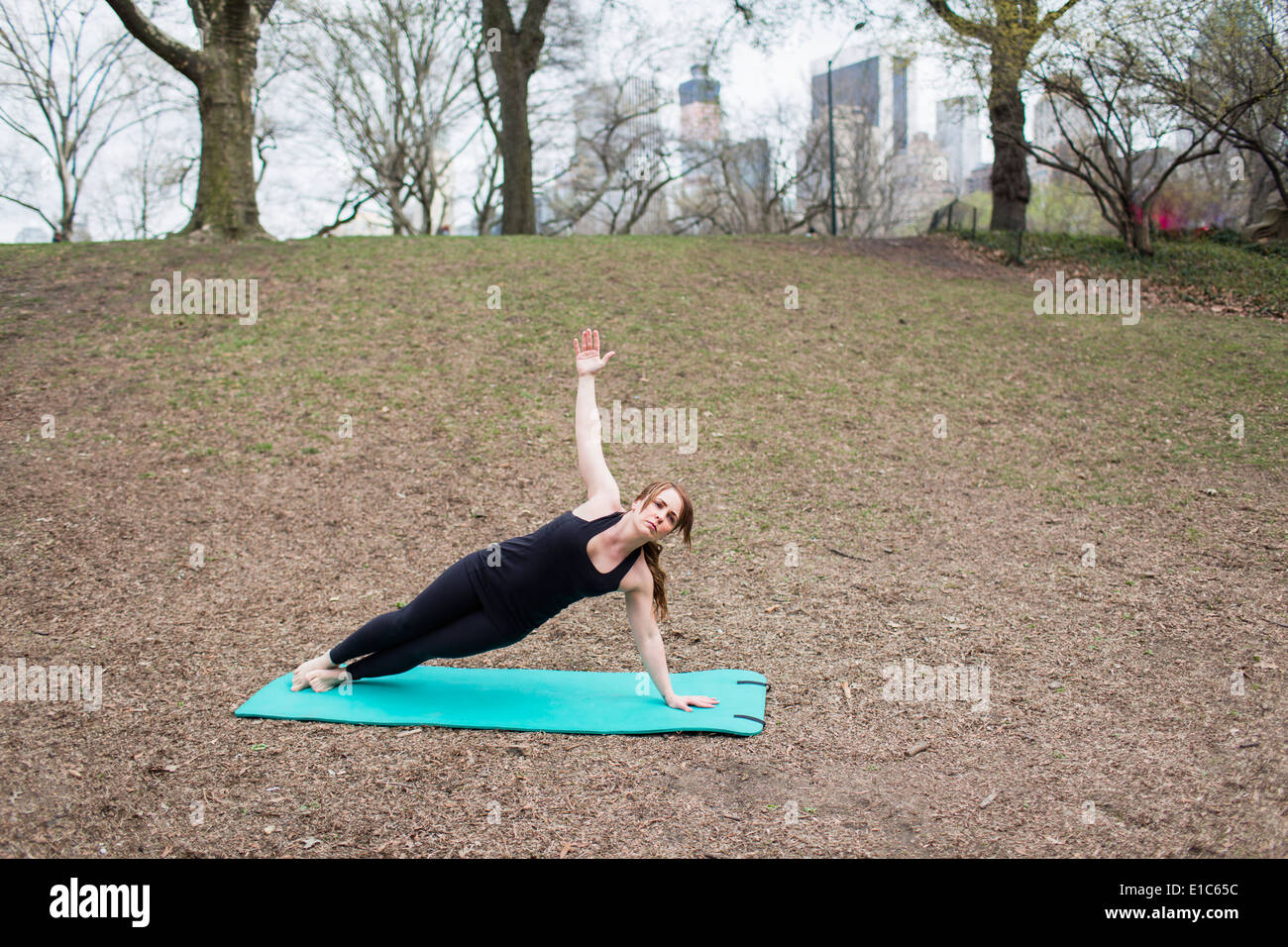 Eine junge Frau im Central Park, in einem schwarzen Anzug und Leggings, Yoga zu tun. Stockfoto