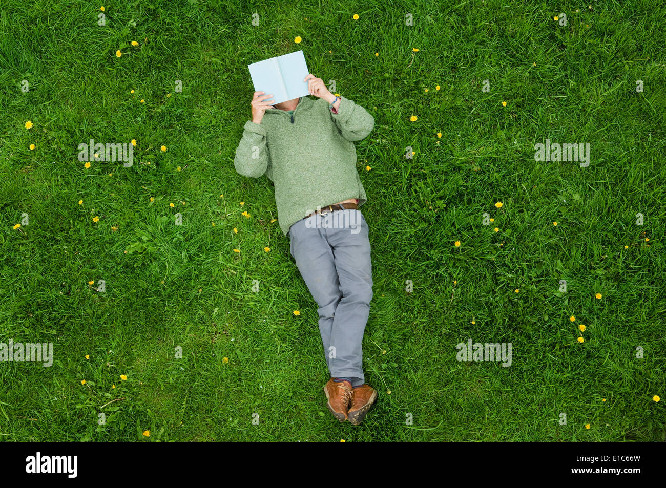 Ein Mann auf dem Rücken im Gras liegend ein Buch lesen. Stockfoto
