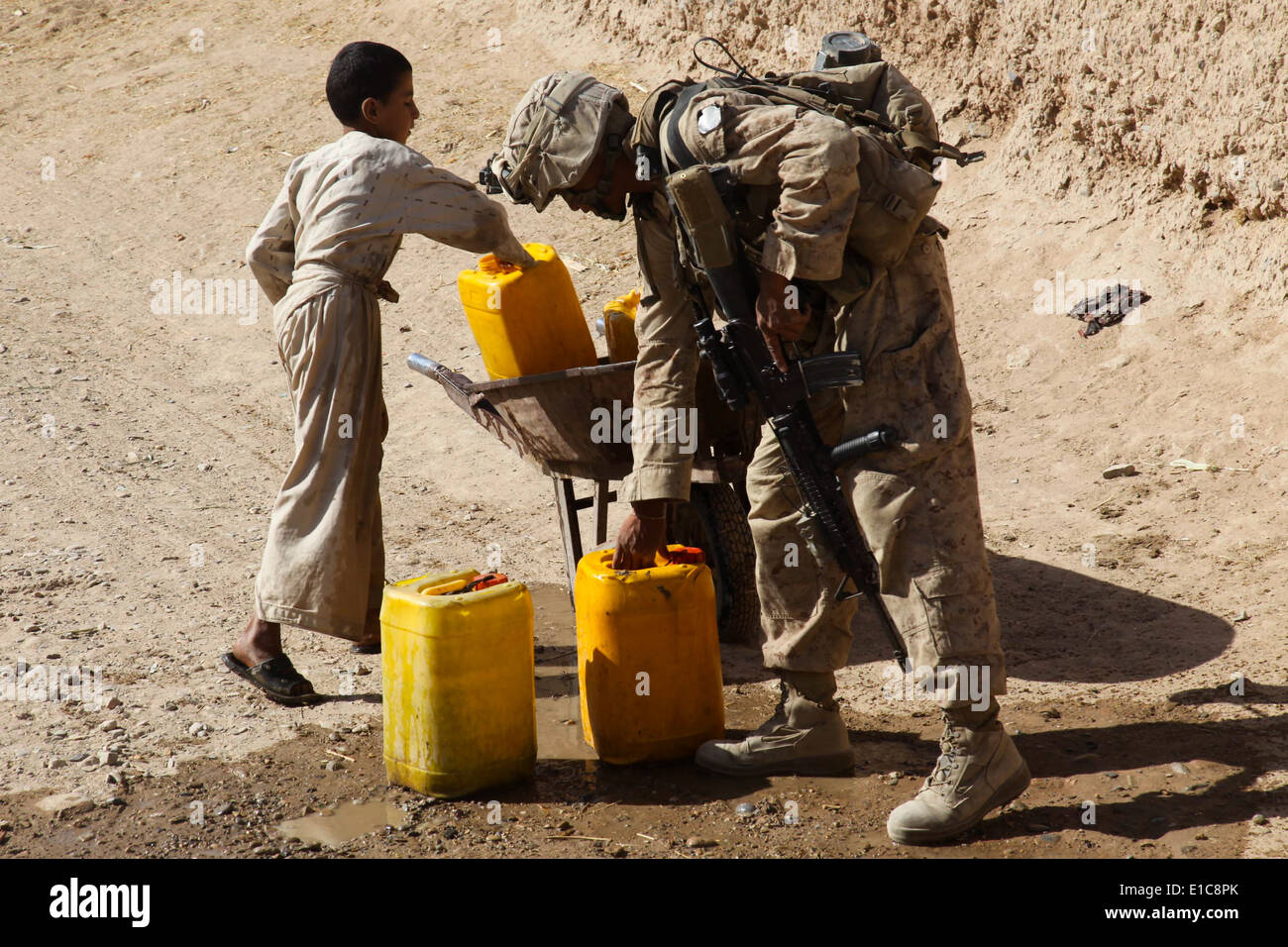 U.S. Marine Corps Lance Cpl. Kevin Choeun hilft einen afghanischen junge seiner Schubkarre mit Krügen Wasser während einer Patrouille in der Naw laden Stockfoto