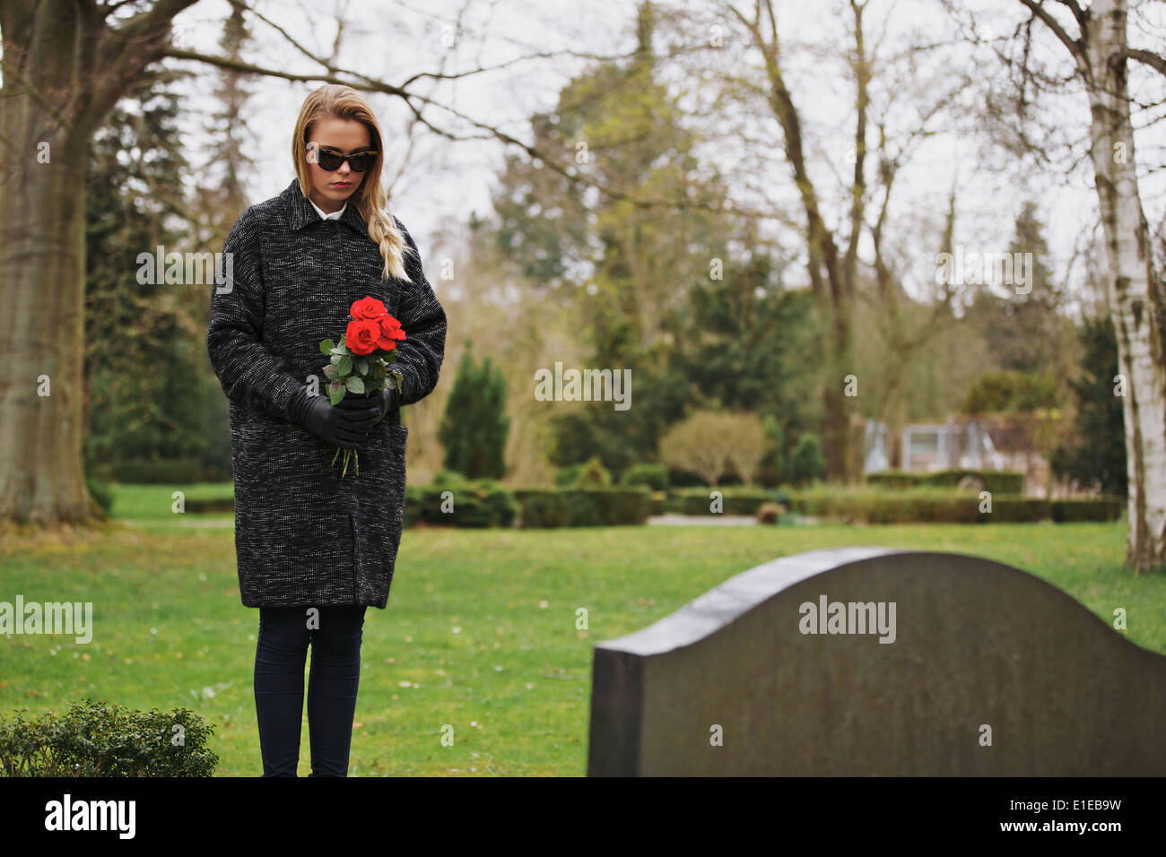 Junge Frau am Grab eines verstorbenen Familienmitglieds stehen. Frau am Friedhof trauernde Blumen halten. Stockfoto