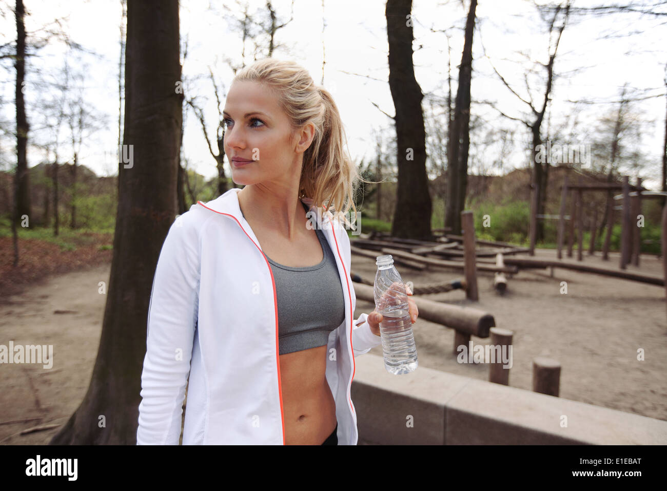 Junge Frau im Park mit Wasserflasche wegsehen. Fitness-Frau nach Training in der Natur entspannen. Stockfoto