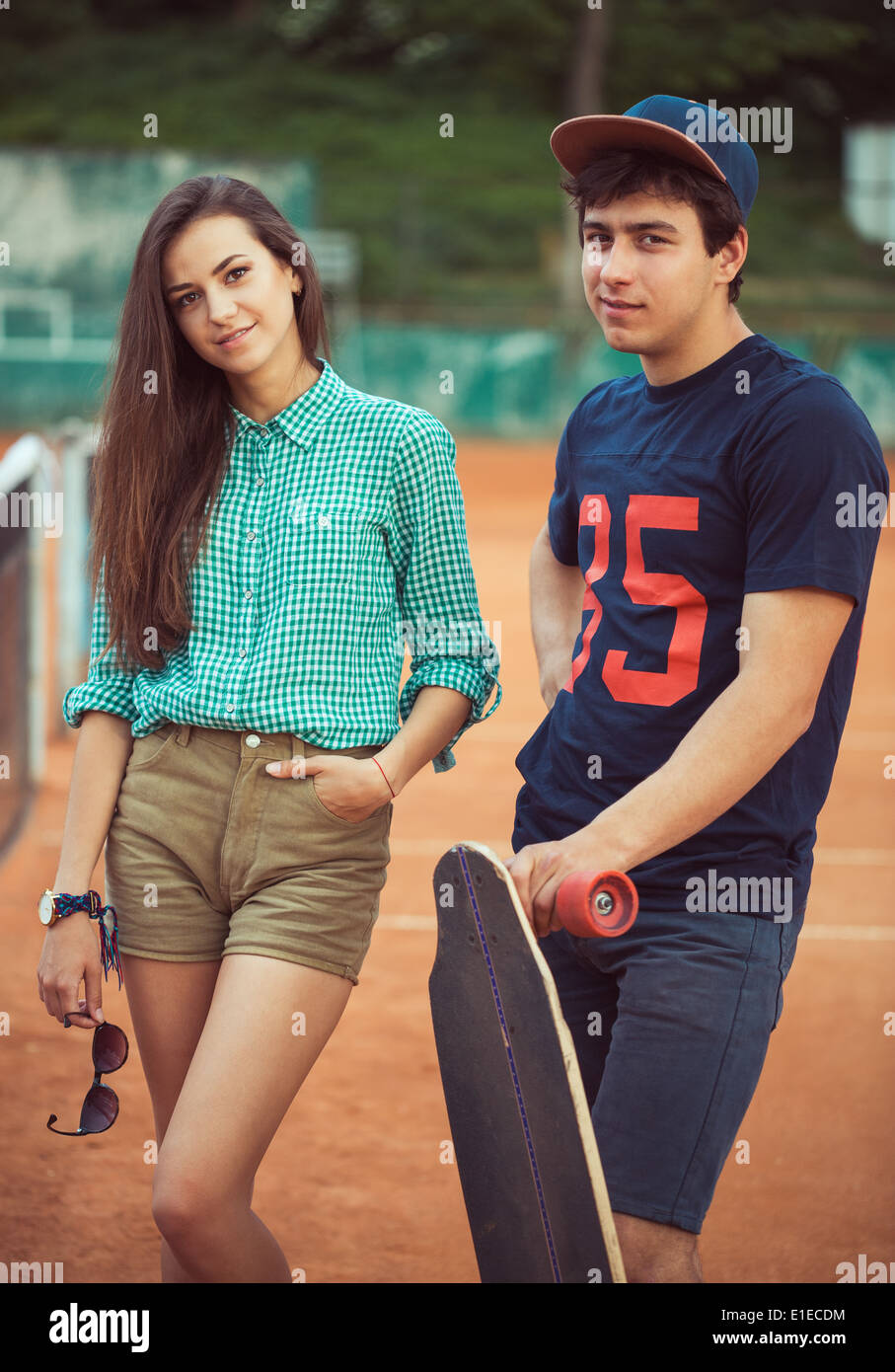Junge schöne Paar stehend auf einem Skateboard auf dem Tennisplatz Stockfoto