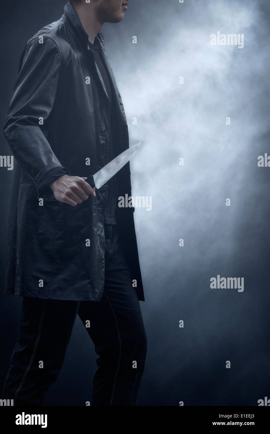 ein Mann in dunkler Kleidung mit einem Messer Stockfoto