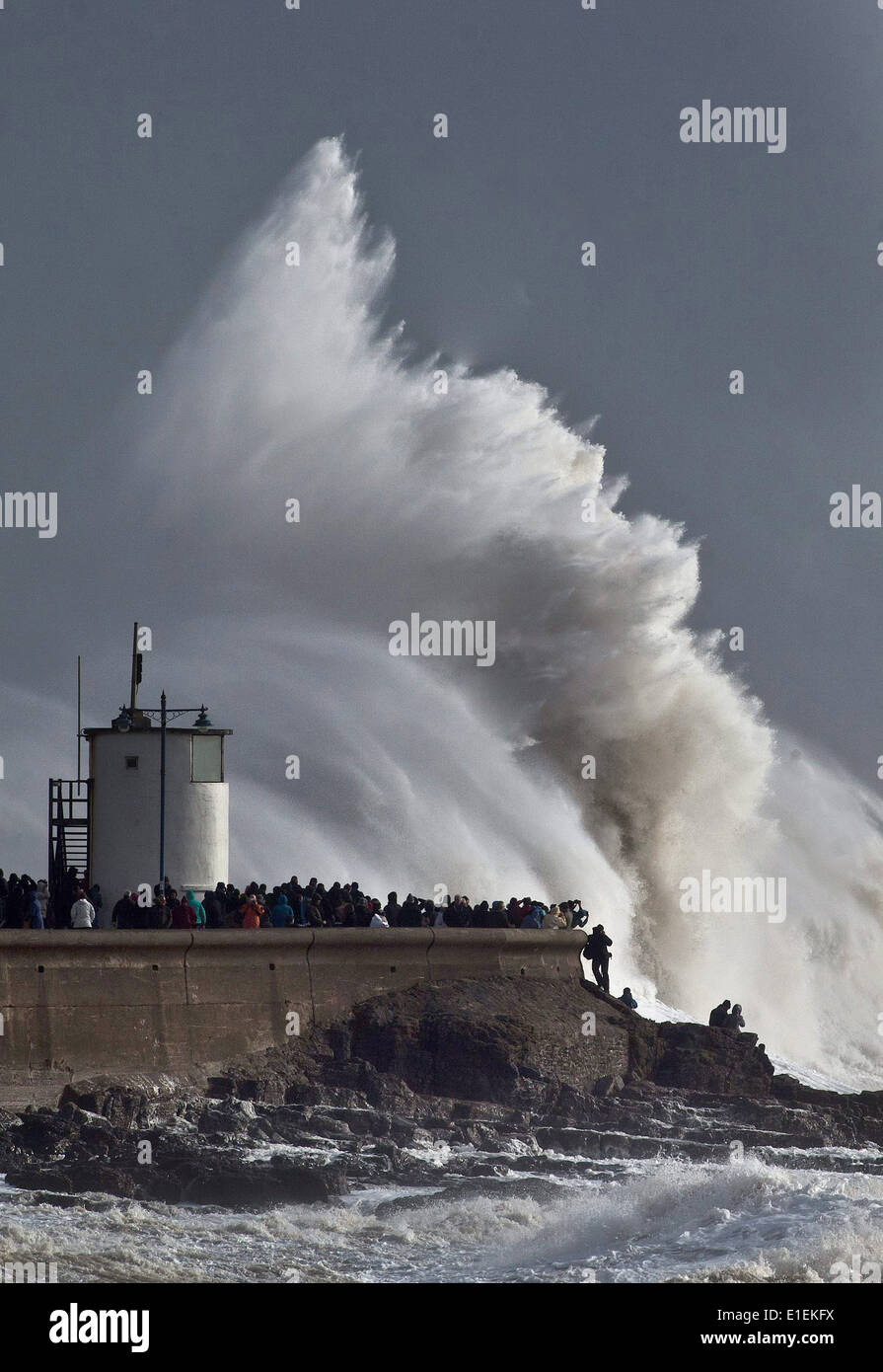 Dutzende von Menschen packen die Ufermauer in Porthcawl in Süd-Wales, die massiven Wellen schlagen den Leuchtturm zu sehen Stockfoto