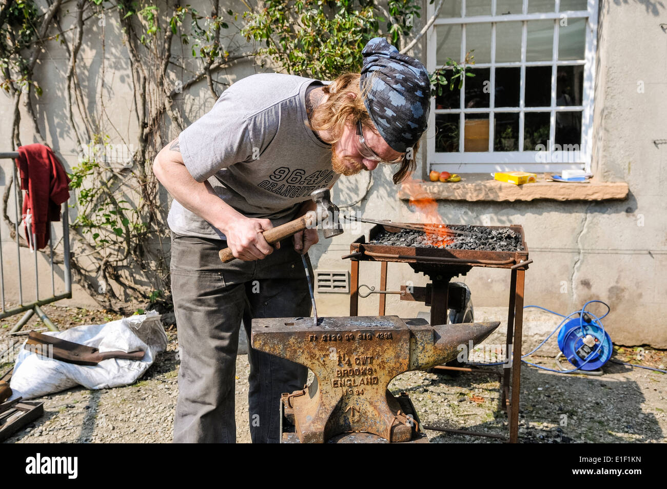 Schmied benutzt einen Hammer und Amboss, eine Eisenstange zu gestalten Stockfoto
