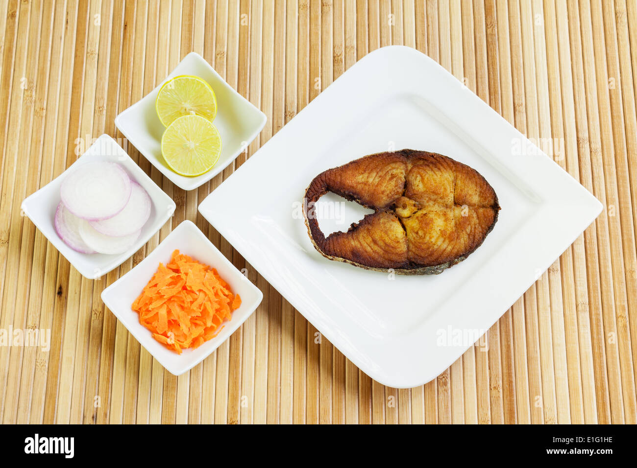 Lecker, knusprig gebratene, verkrusteten Seher/Makrele Fisch Filet mit geriebenen Karotten, rohe Zwiebelringe und Zitrone serviert. Stockfoto