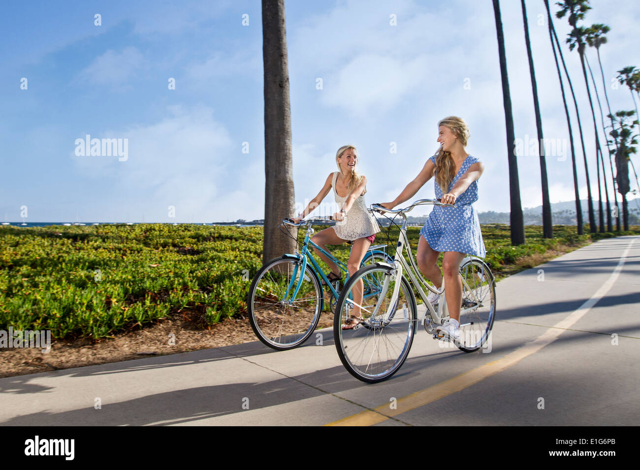 Zwei Frauen, die ihre Fahrräder auf dem Radweg am Strand Reiten. Die Frauen sind in Sommerkleidung lachend, als sie zu reiten. Stockfoto
