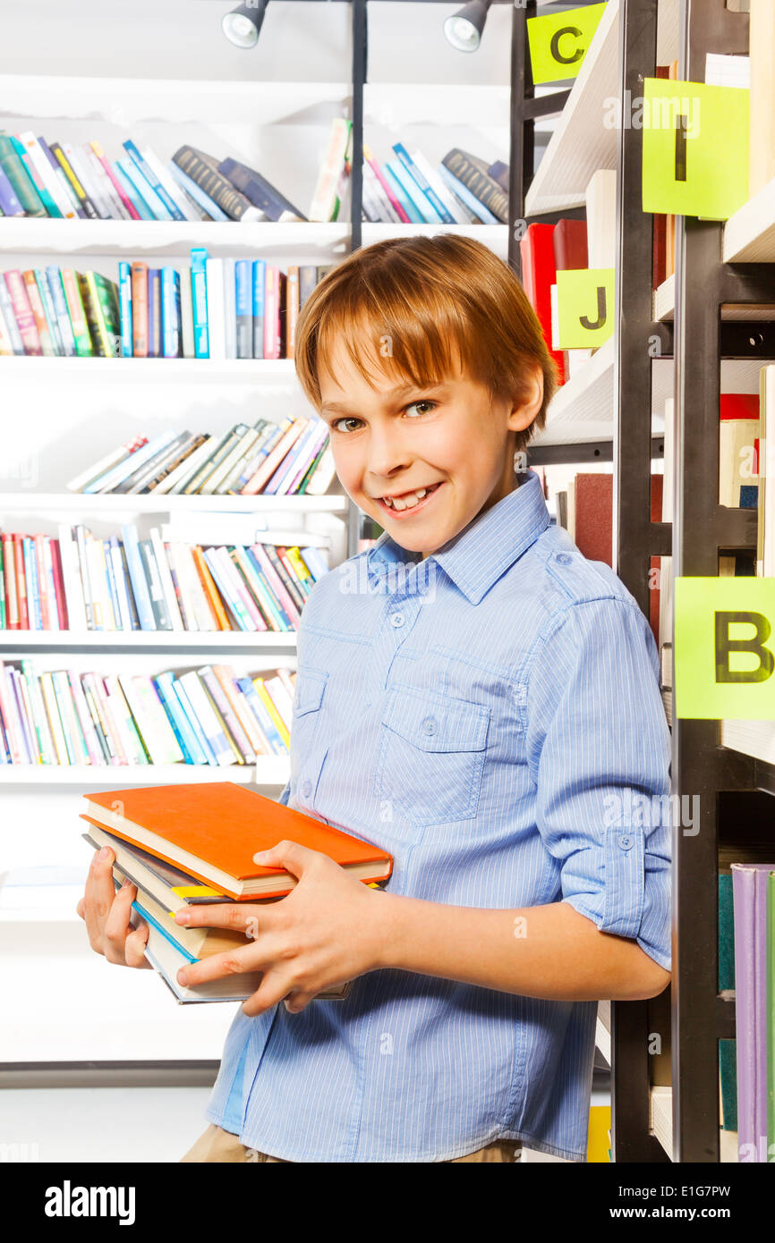 Schuljunge steht und hält Bücher in der Bibliothek Stockfoto