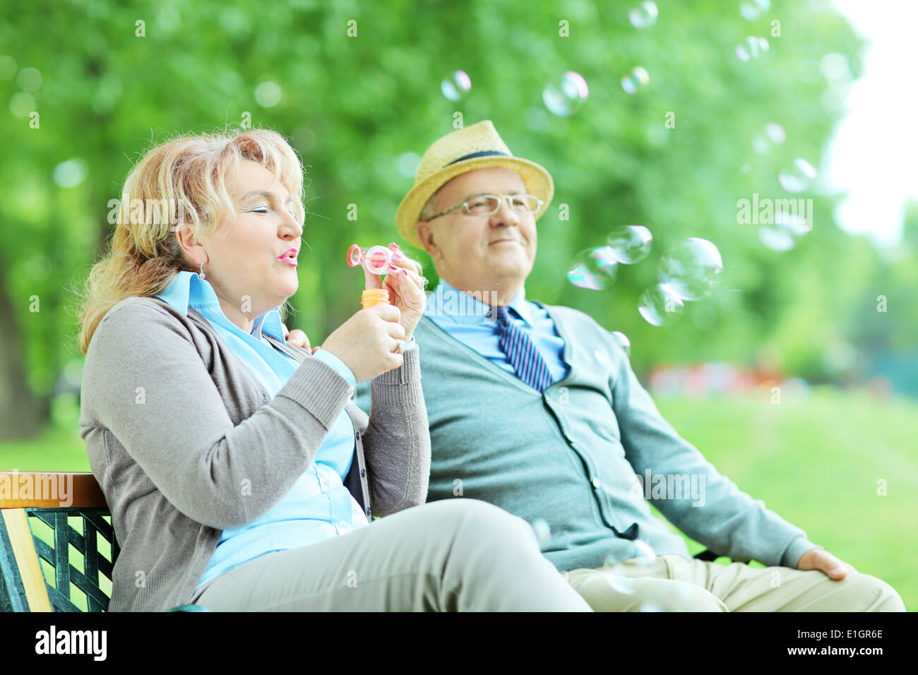 Unbeschwerte älteres paar Seifenblasen auf Bank im Park sitzend Stockfoto